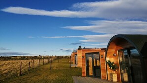 A modern wooden cabin with a large glass door and a curved roof, surrounded by a fenced field. - Hillhead Hideaways (Keith)