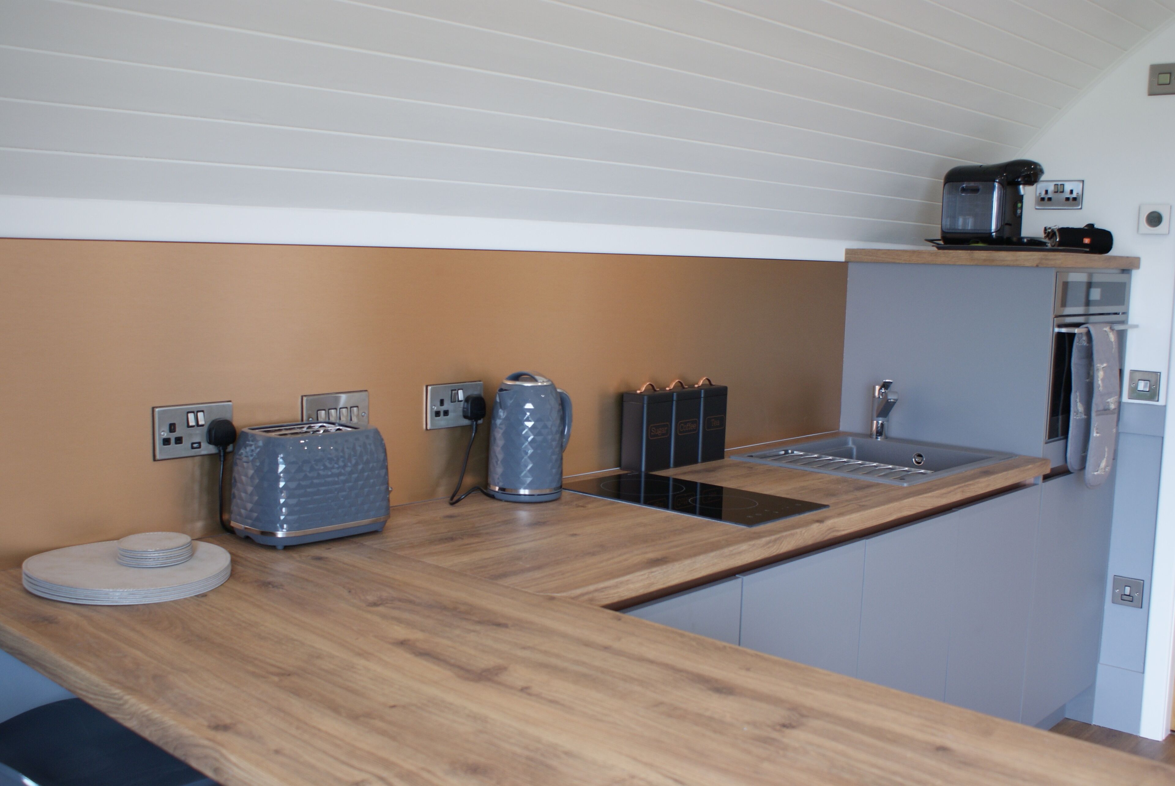 A compact kitchen with a wooden countertop, a built-in sink, and a coffee machine.