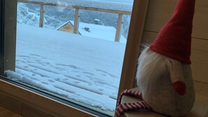A window with a view of a snowy landscape and a wooden deck. - Beautiful Chalet "Hygge" (venosc)