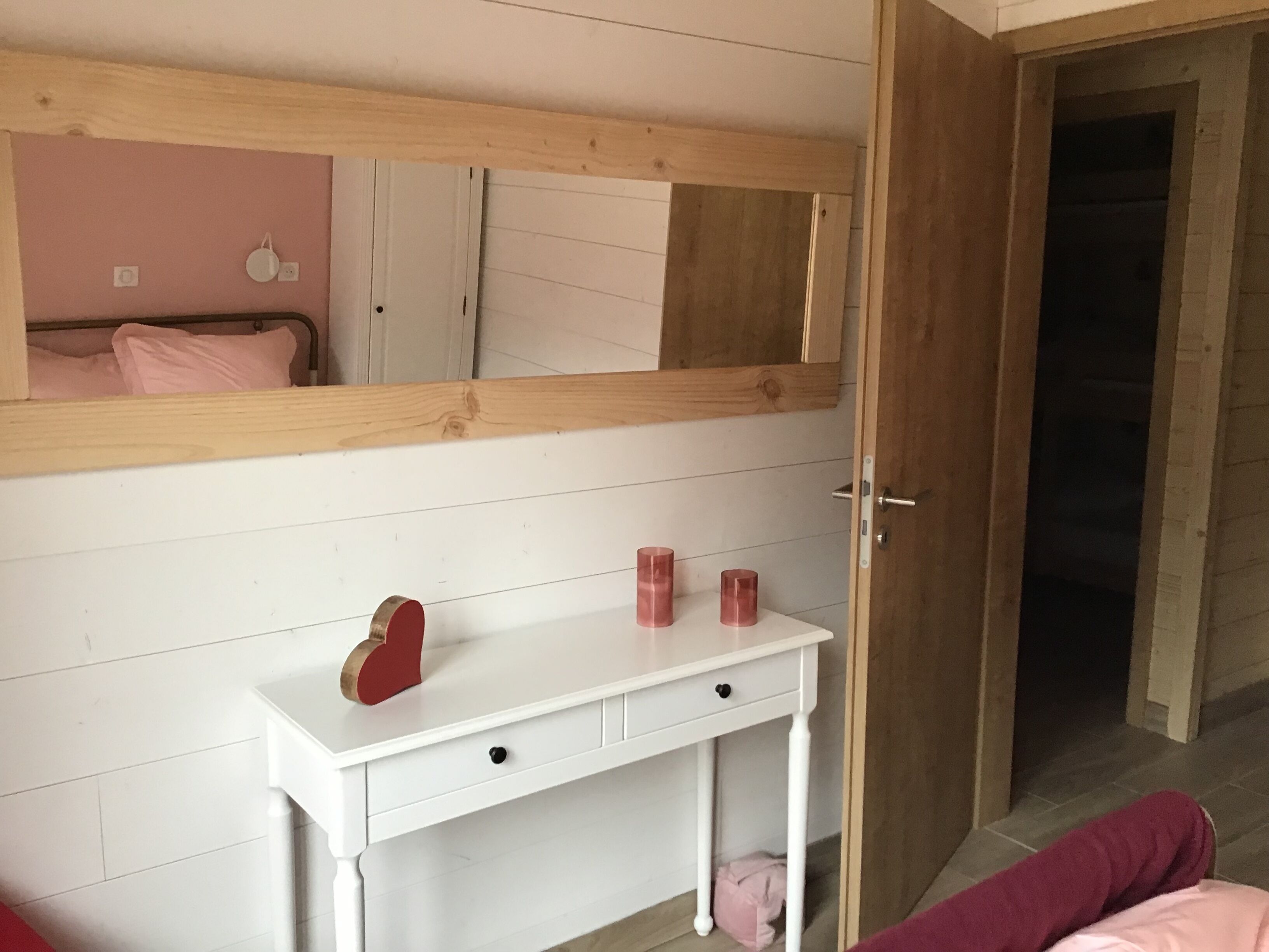 Une chambre avec une commode blanche, un miroir au-dessus, et une porte donnant sur une autre pièce.
