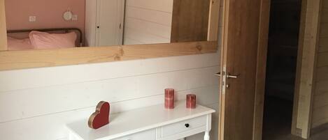 Une chambre avec une commode blanche, un miroir au-dessus, et une porte donnant sur une autre pièce.