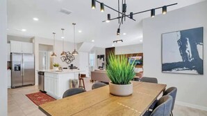 Una cocina moderna con una isla central, iluminación colgante y un comedor con mesa y sillas de madera.