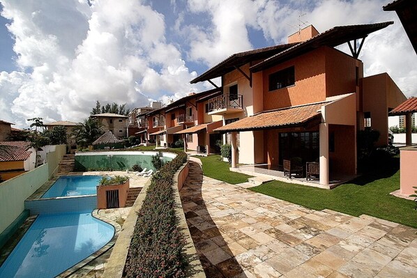 A residential building with a swimming pool, a well-maintained lawn, and a clear sky.