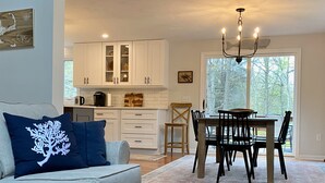 A modern living room with a grey sofa, a dining table with chairs, and a kitchen in the background. - Lovely three bedroom home located in desirable Bayside neighborhood! (South Dennis)