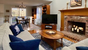 A living room with a fireplace, a television, and a dining area with a table and chairs. - Lovely three bedroom home located in desirable Bayside neighborhood! (South Dennis)