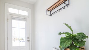 En stilren, modern entré med en träbänk, en flätad korg med en växt och en vit dörr.