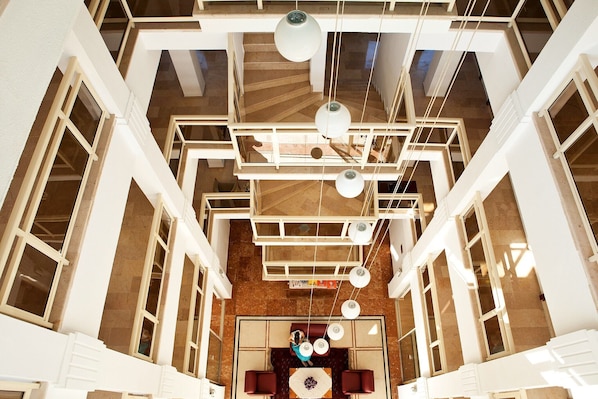 A high-ceiling atrium with a central seating area, multiple staircases, and hanging pendant lights.