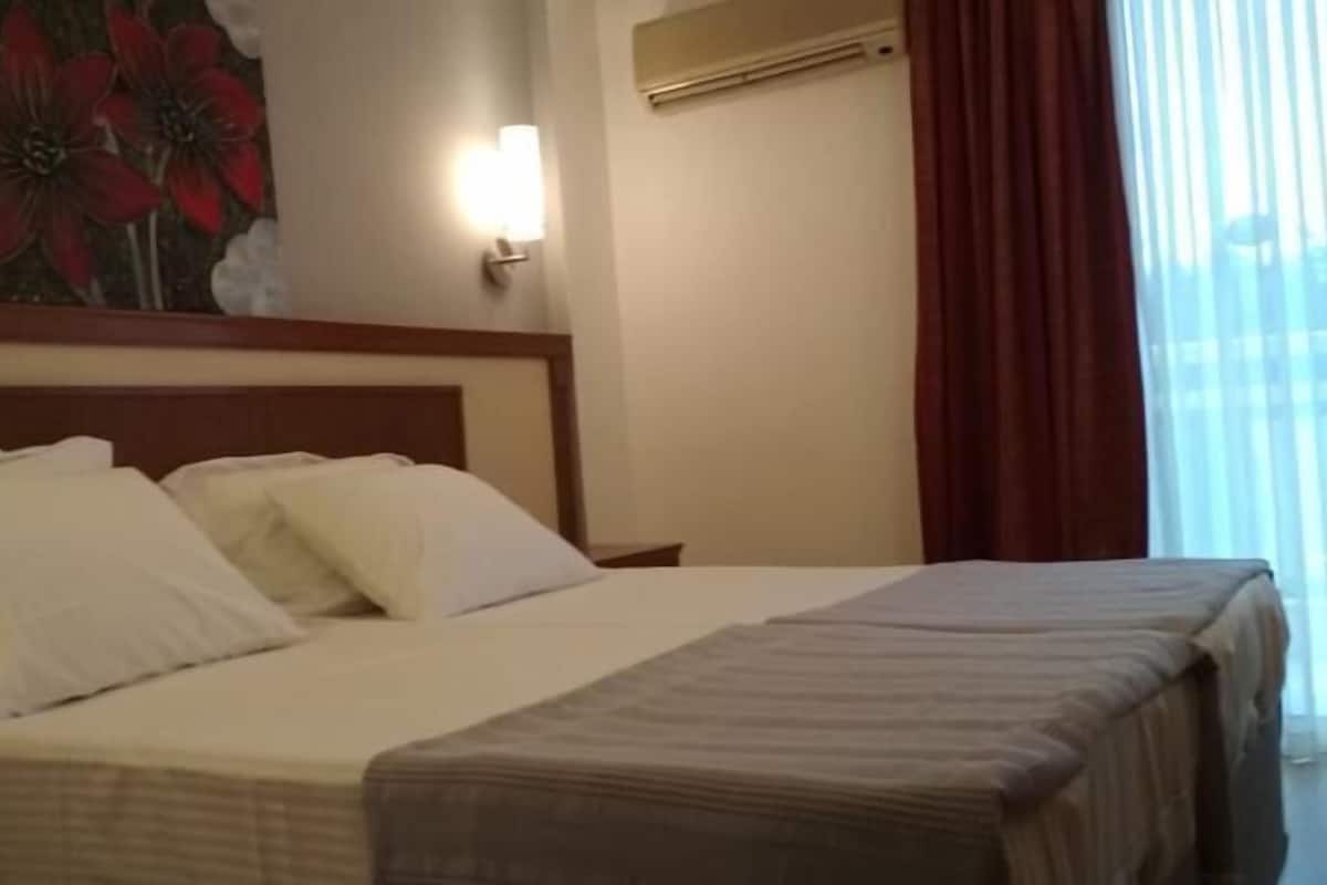 A hotel room with a bed, a nightstand, a wall-mounted lamp, and a window with curtains.
