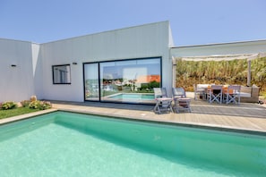 A modern house with a swimming pool, a deck with outdoor furniture, and a large glass window. - Ericeira - House with a Garden and Pool (Ericeira)