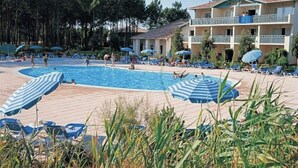 A pool area with lounge chairs and umbrellas, surrounded by a building with balconies.
