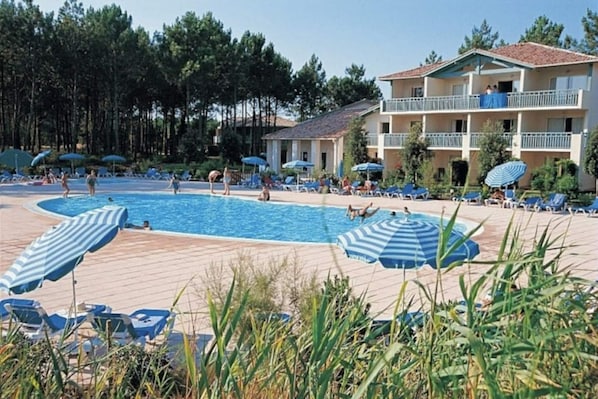 A pool area with lounge chairs and umbrellas, surrounded by a building with balconies.