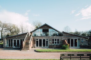 A wooden cabin with a glass extension, outdoor seating, and a gravel driveway. - Elmbridge Farm Nuthatch Lodge (Droitwich)