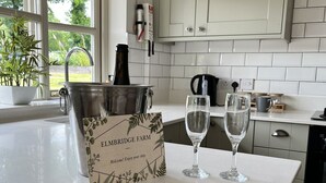 Una cocina con mostrador blanco, una planta en maceta, una botella, una copa de vino y un cartel de bienvenida.