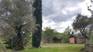 A rustic stone building with a wooden door, surrounded by lush greenery and trees. - Comfortable house in the Pyrenees with views (Ainsa-Sobrarbe)