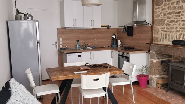 Une cuisine de taille réduite avec des meubles blancs, un plan de travail en bois et un mur en pierre.