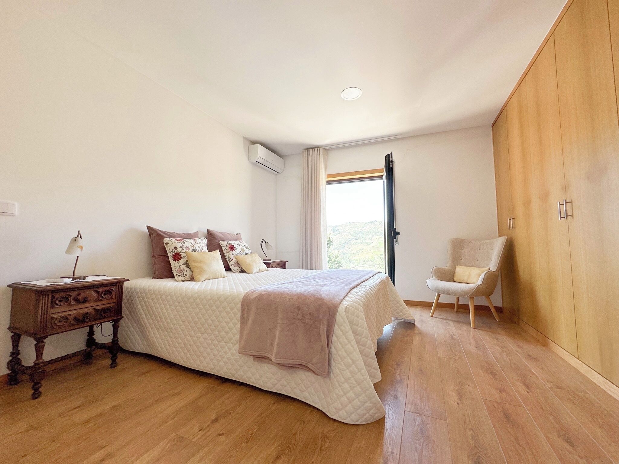 Une chambre à coucher comprenant un lit, une table de chevet, une chaise, une armoire et une fenêtre donnant sur un paysage agréable.