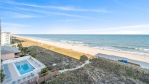Une vue sur la plage avec un espace piscine, une plage de sable et l’océan.