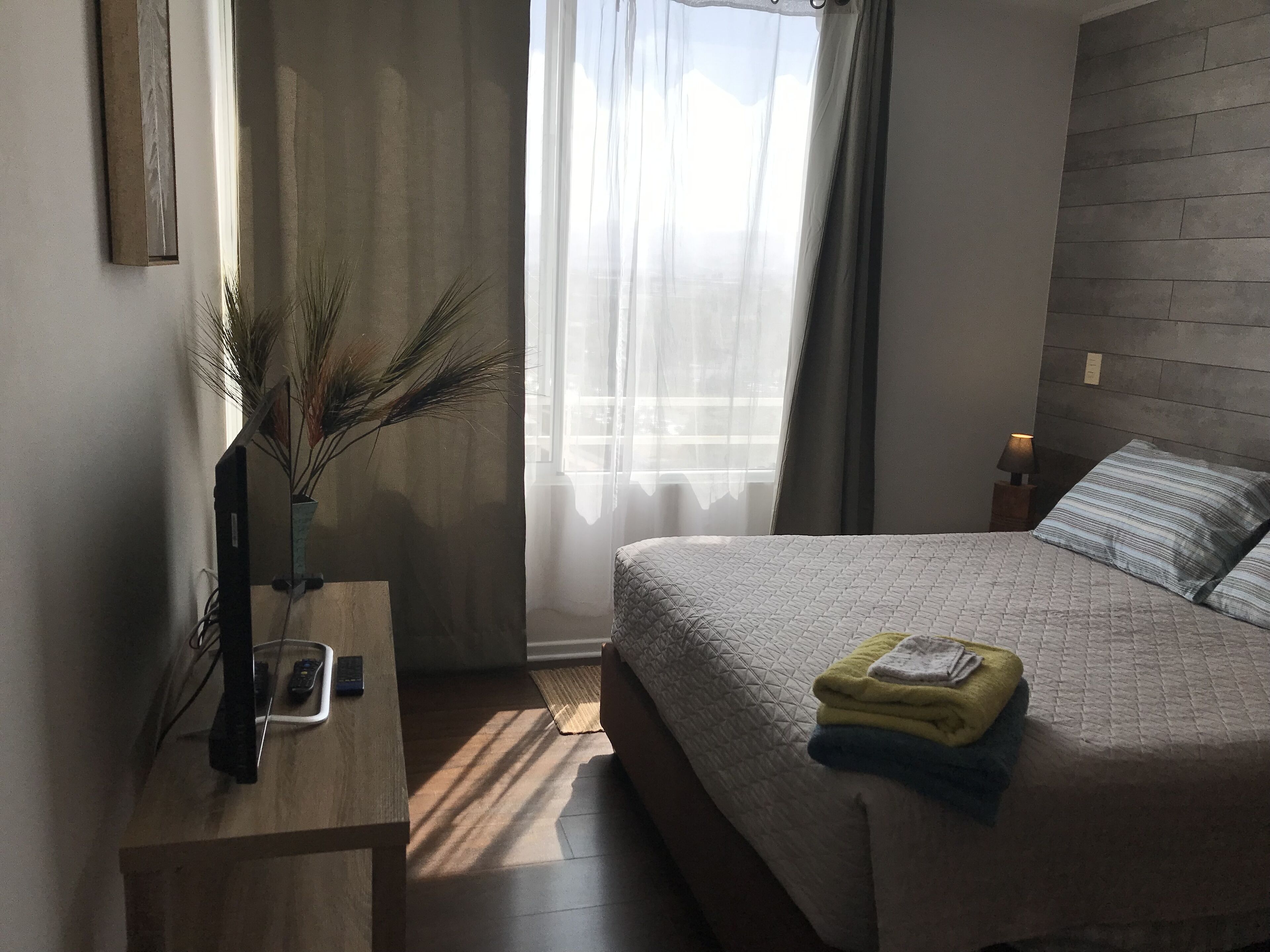 A bedroom with a bed, bedside table, lamp, and a window with curtains.