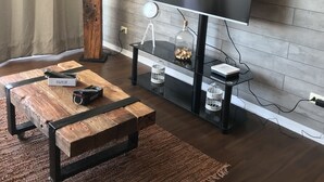 A modern living room with a large flat-screen TV mounted on a brick wall, a wooden coffee table with a lamp, and a glass-top side table with decorative items.