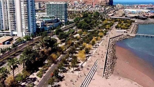A coastal cityscape with high-rise buildings, a beach promenade, and a rocky coastline.