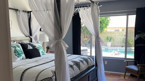 A bedroom with a four-poster bed, a ceiling fan, and a view of a swimming pool through large windows. - Diamond in the Desert💎🏝HEATED/COOLED Pool and Spa NO EXTRA CHARGE (Peoria)