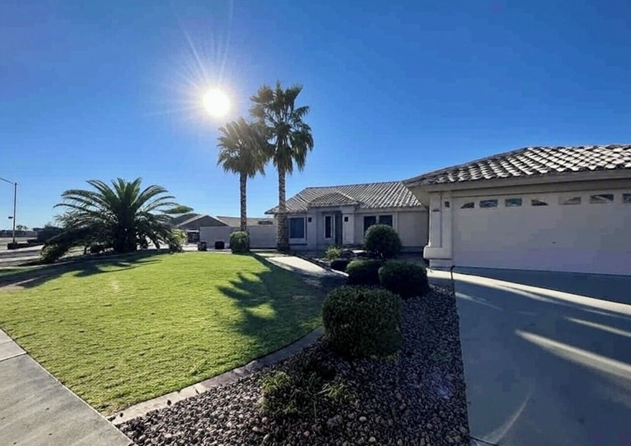 A residential area with a well-maintained lawn, a palm tree, and a house with a tiled roof.