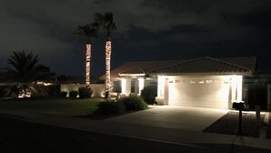 A residential house at night with illuminated exterior lighting, a garage, and a well-maintained lawn. - Diamond in the Desert💎🏝HEATED/COOLED Pool and Spa NO EXTRA CHARGE (Peoria)