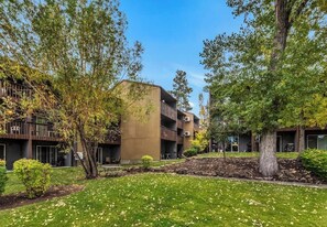 A modern building with multiple balconies, surrounded by trees and a well-maintained lawn.