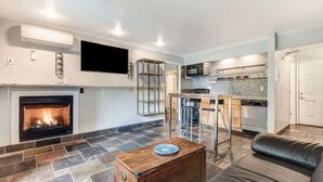 Un salon avec une cheminée, une cuisine avec un dosseret carrelé et un téléviseur à écran plat fixé au mur.