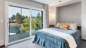 Une chambre avec une grande porte-fenêtre coulissante donnant sur un balcon, un lit avec de nombreux oreillers et une petite table de chevet.