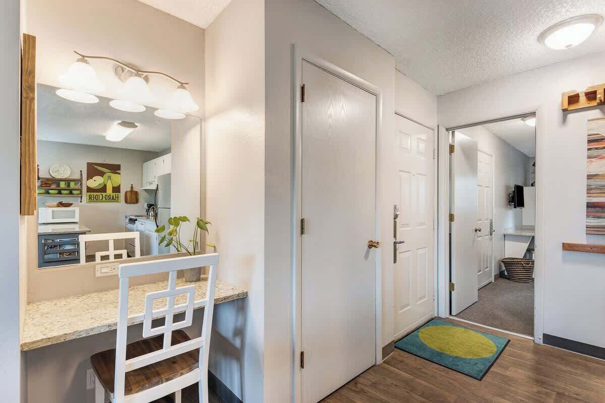 A hallway with a white door, a small rug, and a kitchen area with a microwave and a plant.