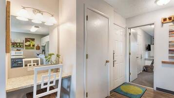 A hallway with a white door, a small rug, and a kitchen area with a microwave and a plant.