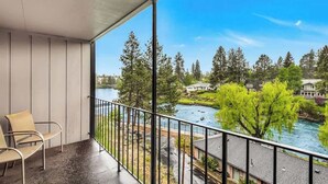 A balcony with chairs, a view of a river, trees, and houses.