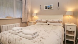 Une chambre à coucher comprenant un lit, deux tables de chevet, une fenêtre avec des rideaux et des lampes fixées au mur.