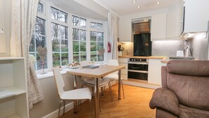 Une cuisine moderne avec des meubles blancs, une table à manger en bois et un canapé en cuir marron.