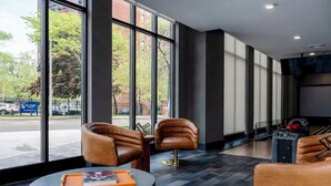 Un vestíbulo moderno con sillones de cuero, una mesa redonda con un libro y un ventanal con vistas a la calle y árboles.