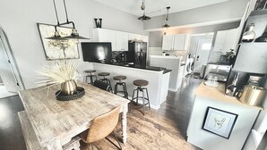 A modern kitchen with a wooden dining table, bar stools, a TV, and a central island. - Hot Tub Beautiful Downtown Indy Home! (Indianapolis)