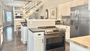 A modern kitchen with a stainless steel stove, white cabinets, and a large refrigerator. - Hot Tub Beautiful Downtown Indy Home! (Indianapolis)