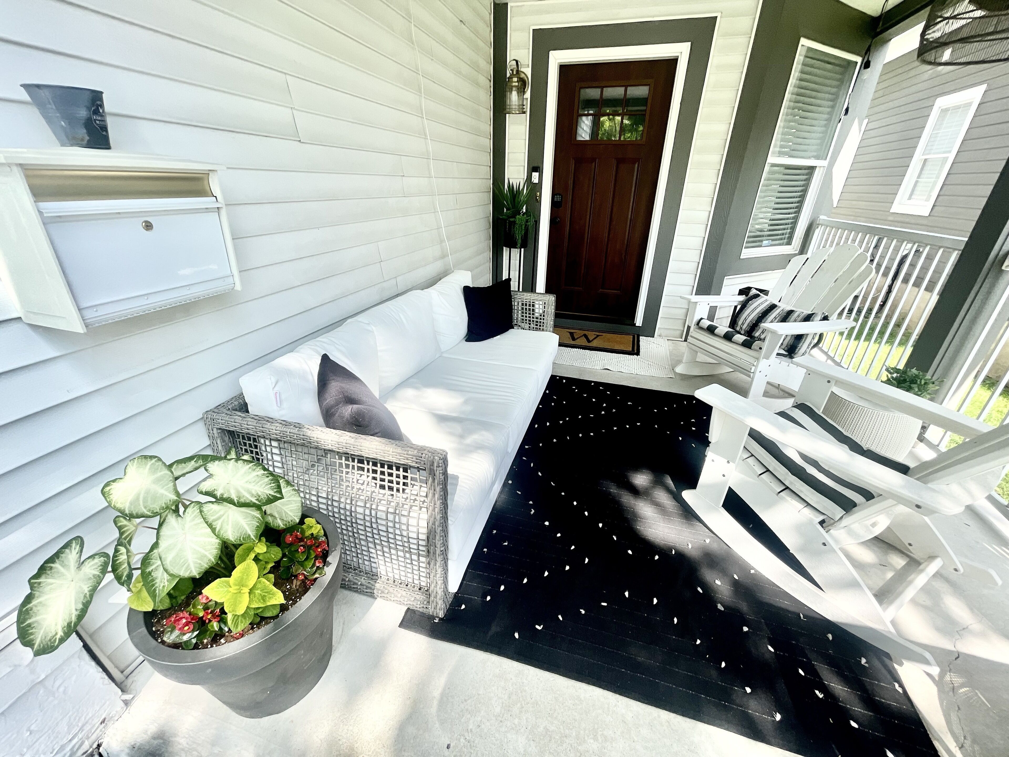 A white porch with a black rug, white furniture, and a potted plant.