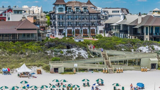 Et strandhotel med et markant tårn, en træpromenade ned til stranden og strandparasoller.