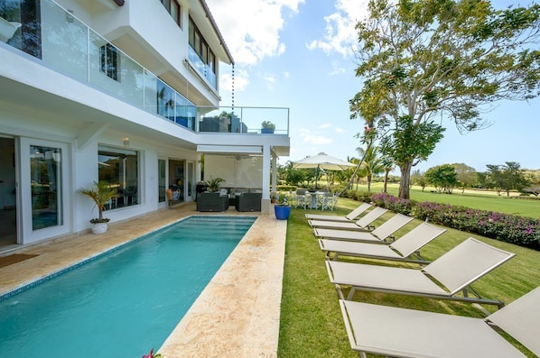 A modern two-story house with a swimming pool, outdoor seating, and a well-maintained lawn.