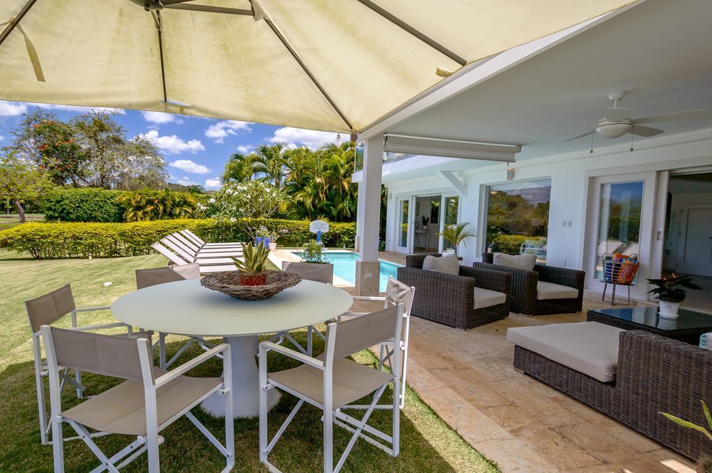 An outdoor patio with a round table and chairs, a pool, and wicker furniture.