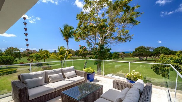A balcony with wicker furniture, a glass table, and potted plants. - Private Villa with Pool and Golf Cart (San Rafael del Yuma)