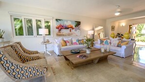 A living room with a sofa, armchairs, and a coffee table. There are plants, a painting, and a lamp on the walls. - Private Villa with Pool and Golf Cart (San Rafael del Yuma)