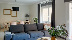 Un soggiorno moderno con un divano grigio, un tavolo da pranzo con sedie, una lampada e una finestra con tende.