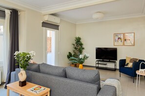 A modern living room with a grey sofa, a coffee table, a TV, and two potted plants. - Casa Cosi - Casanova 1 (Barcelona)