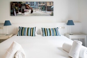 A hotel room with a large bed, striped pillows, two bedside tables with lamps, and a painting on the wall.