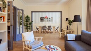 A modern living room with a grey sofa, a wooden chair, a round coffee table, and a dining area with a table and chairs. - Casa Cosi - Casanova 2 (Barcelona)