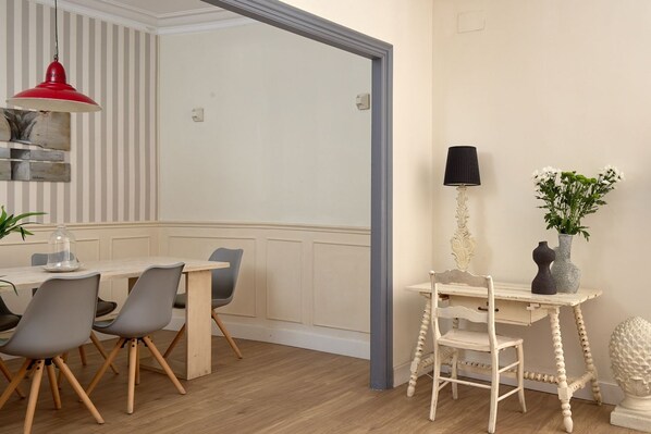A dining area with a wooden table and chairs, a red pendant light, a black lamp, and a vase with flowers.