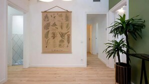 Un couloir au sol en bois, un motif floral sur le mur et une plante en pot.